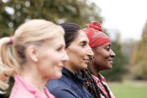 Side portrait of group of fitness mature women in a park. They are multiracial friends and only the black one is in focus. Motivation, happiness and overcoming concept.