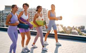 Women in sportswear with rubber mats going to yoga class on roof of house overlooking city and sea. Sport and recreation. Morning exercises in the fresh air. Active and healthy lifestyle.